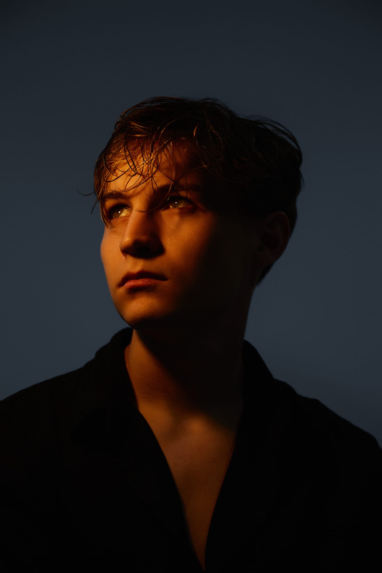 Editorial close-up portrait of BUJA lit with warm amber light against a dark background